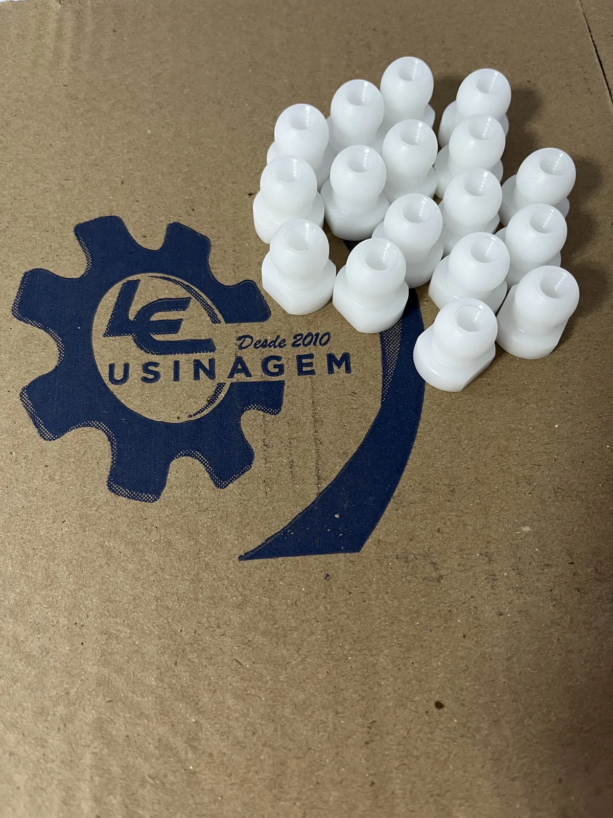 Lote de peças usinadas em plástico de engenharia branco sobre caixa com o logotipo da LE Usinagem